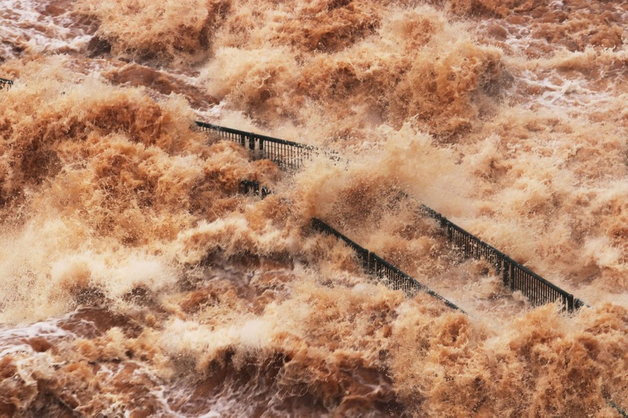 Rushing and splashing river water engulfs a tourist walkway.