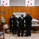 Family members dressed in black stand around a white casket, mourning at a funeral home.