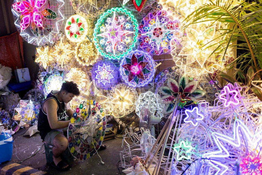 A vendor works on a lantern beside many other lit lanterns hanging on a display wall.