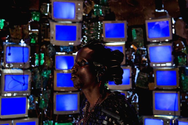 A person staring at stacks of televisions in "Neptune Frost"