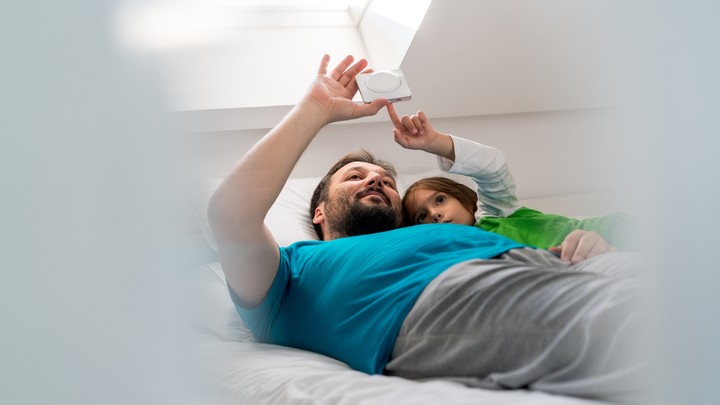 A father and son use an electronic device while lying in bed.