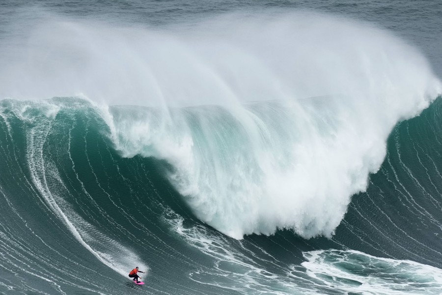 A surfer rides on the lower slope of a massive ocean wave.
