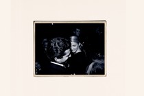 A black-and-white photo of John F. Kennedy Jr. and Carolyn Bessette, against a cream-colored background