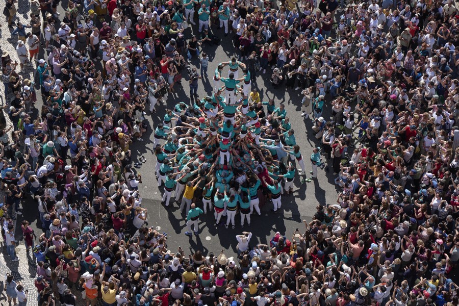 An overhead view of a large crowd gathered around team of people pushing together to make a human tower.