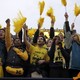 University of Michigan students hold yellow pom-poms and cheer in the stands of a football game. 