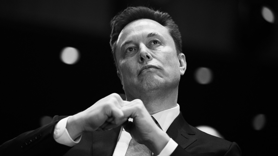 Black-and-white photograph of Elon Musk wearing a suit and tie, looking up.