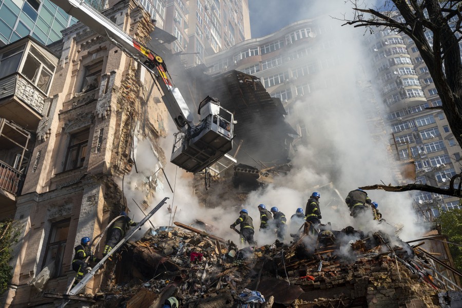 Firefighters work on top of piles of smoking rubble from a destroyed residential building.