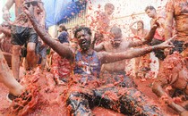 People sit and splash playfully in a large puddle of smashed tomatoes.