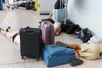 people sprawled out on an airport floor, along with carry-on suitcases