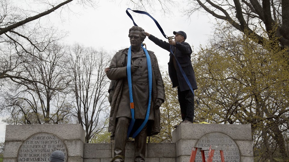 A worker tosses a strap over a statue