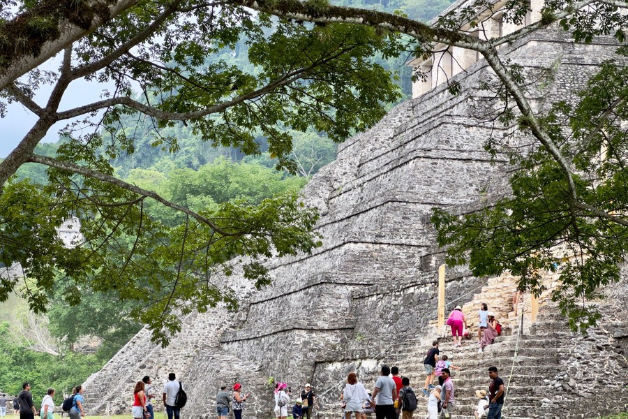 People visit a tall Mayan ruin with a steep facade.