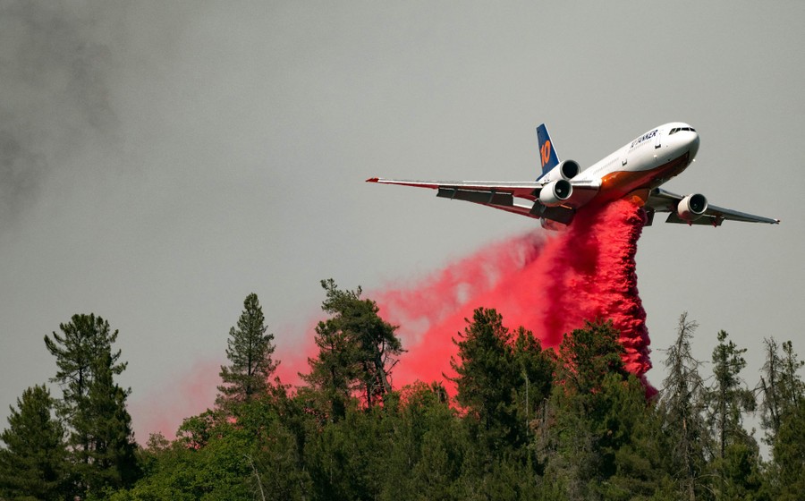 A large aircraft drops fire retardant on a forest.