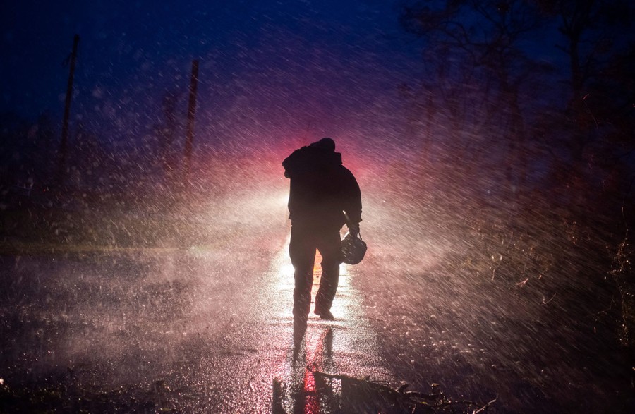 A firefighter walks through strong wind and rain while removing fallen trees at night.