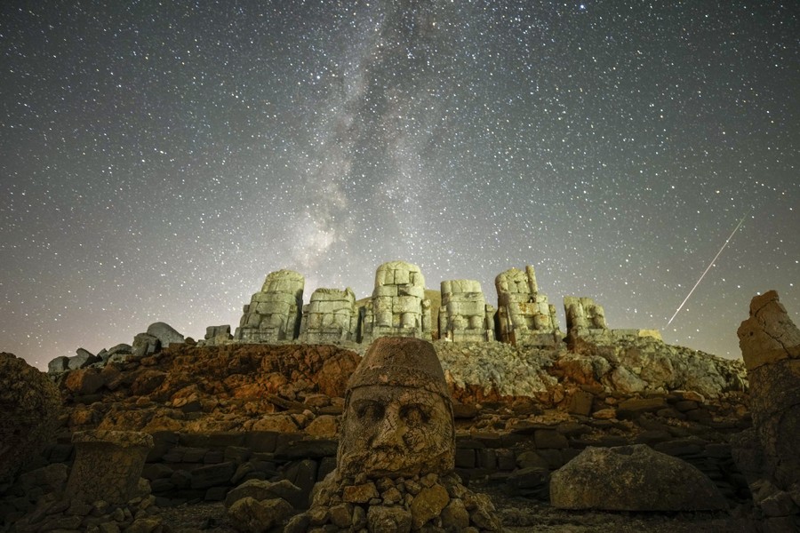 Ancient statues under the starry night sky during a meteor shower