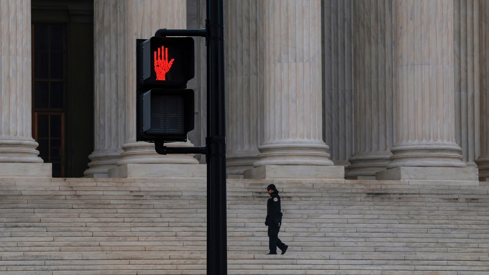 Color photograph of a red "stop" hand sign on a street light outside the Supreme Court building.