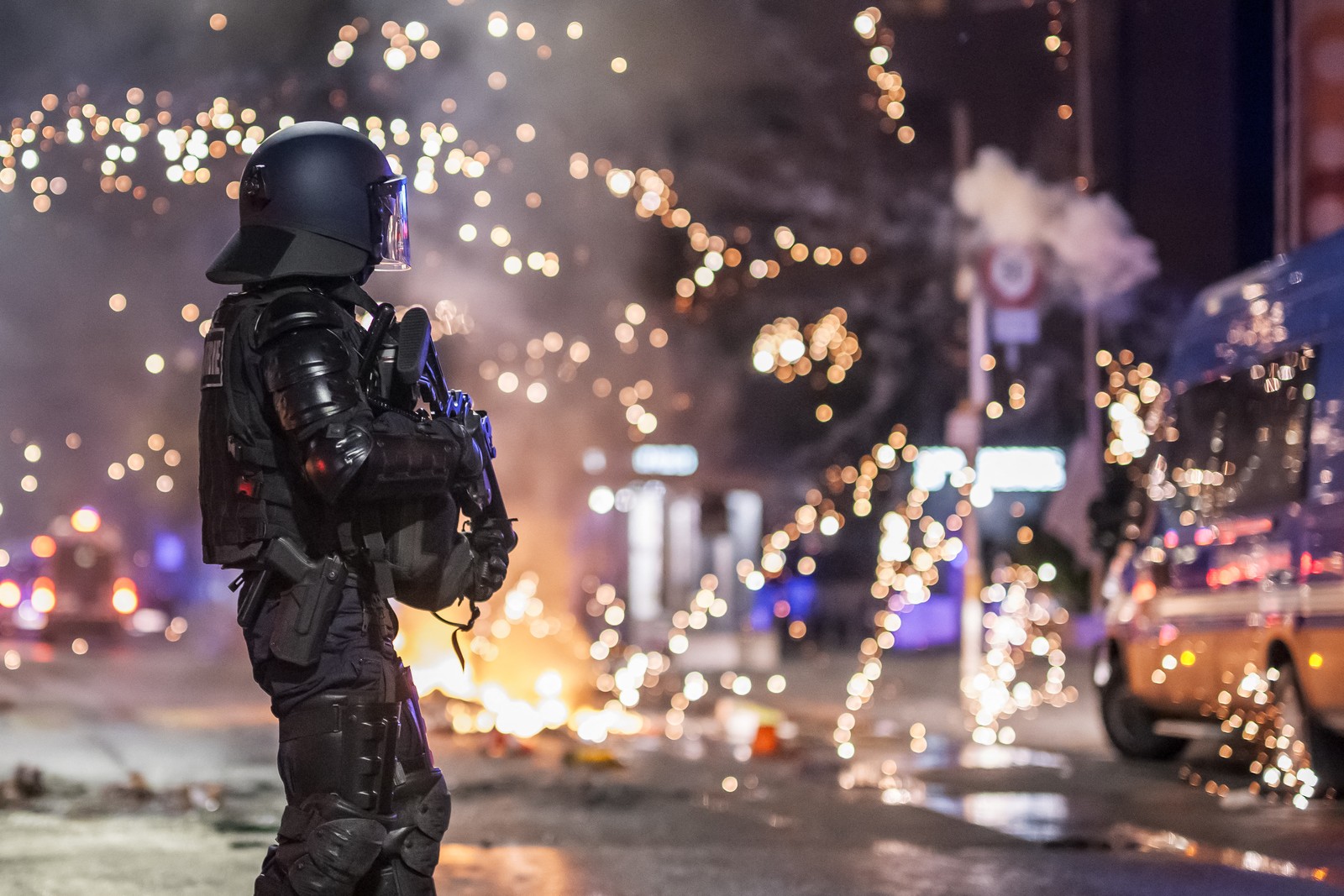 Fireworks explode near a police officer in riot gear.