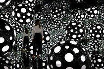A person stands among illuminated spheres in a mirror-walled room.