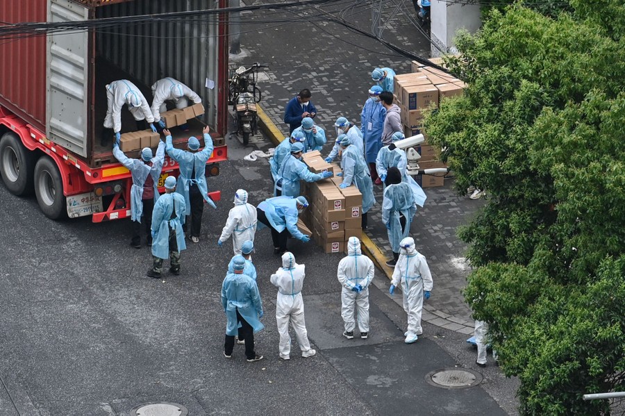 Workers wearing protective gear unload boxes from a truck in a city street.
