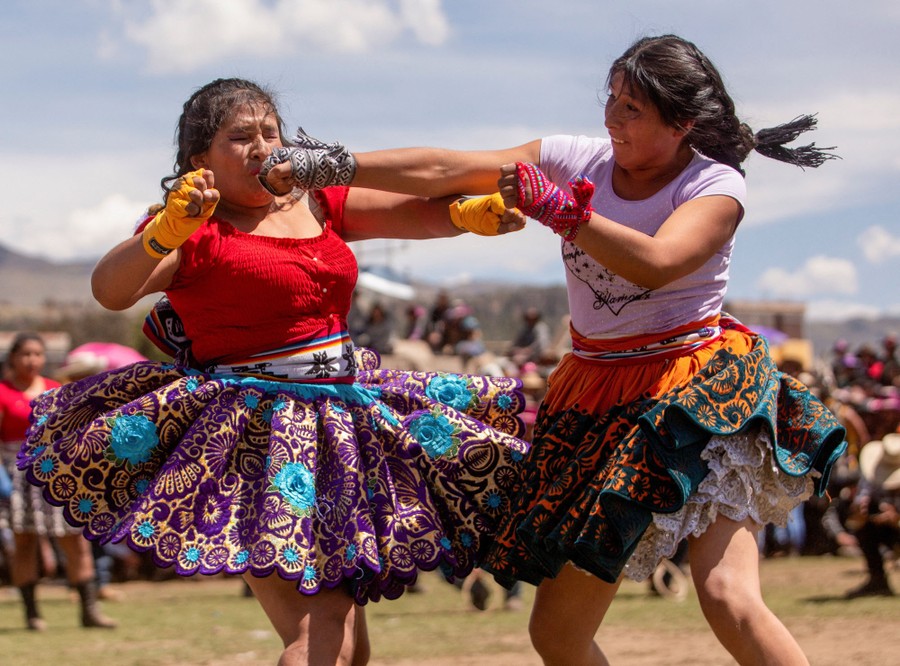 Two women in traditional dress punch each other in a public fight, as others look on.