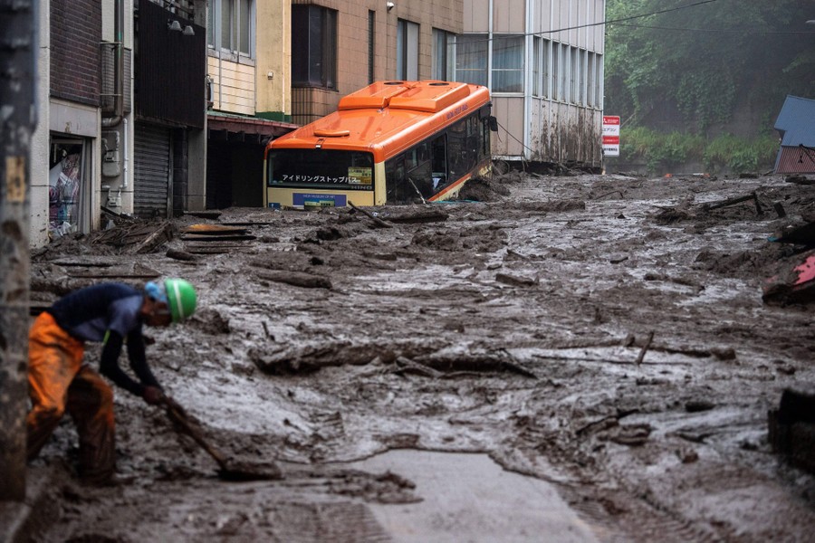 A bus sits stranded in a giant pile of mud that fills a city street.