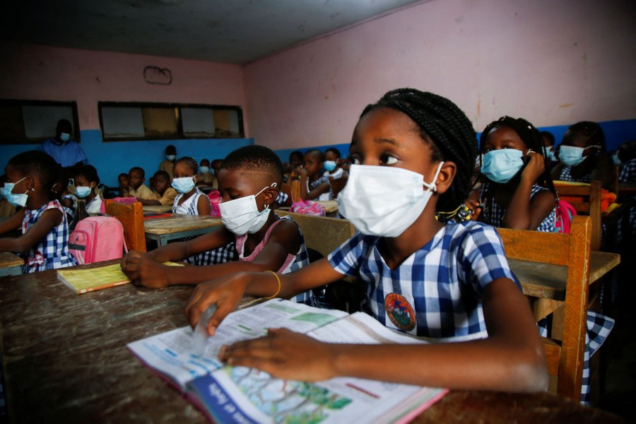 Students wear masks while sitting at desks in a classroom.