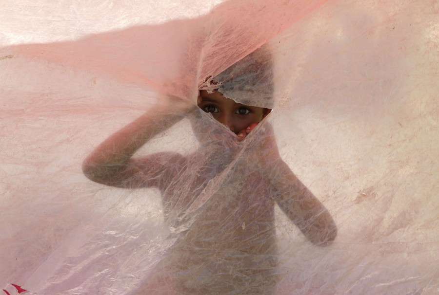 A boy peeks through a tear in a sheet of plastic.