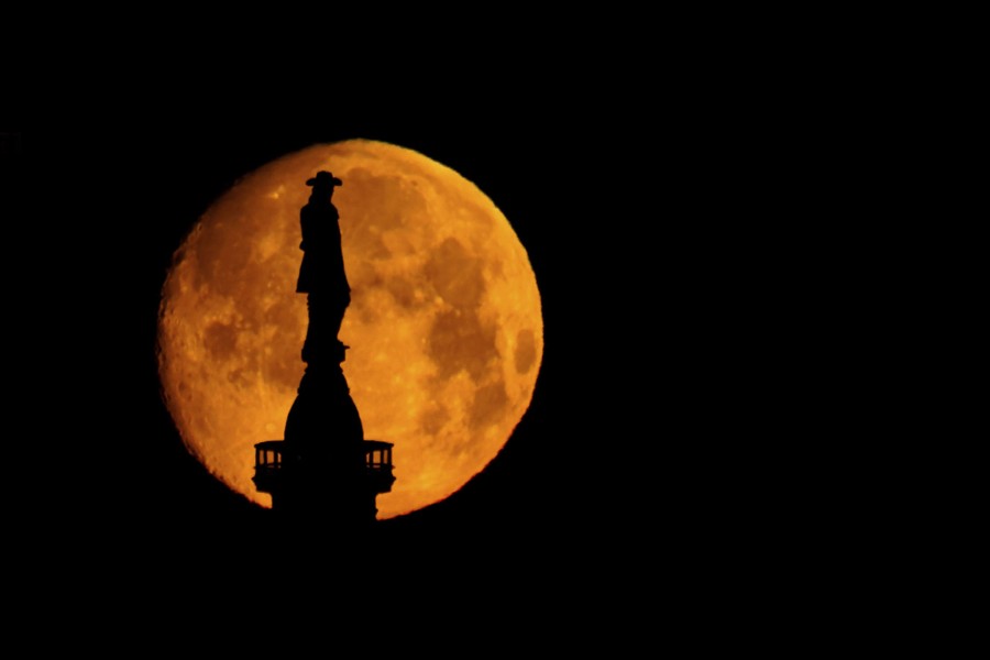 The moon sets behind a statue of a man.
