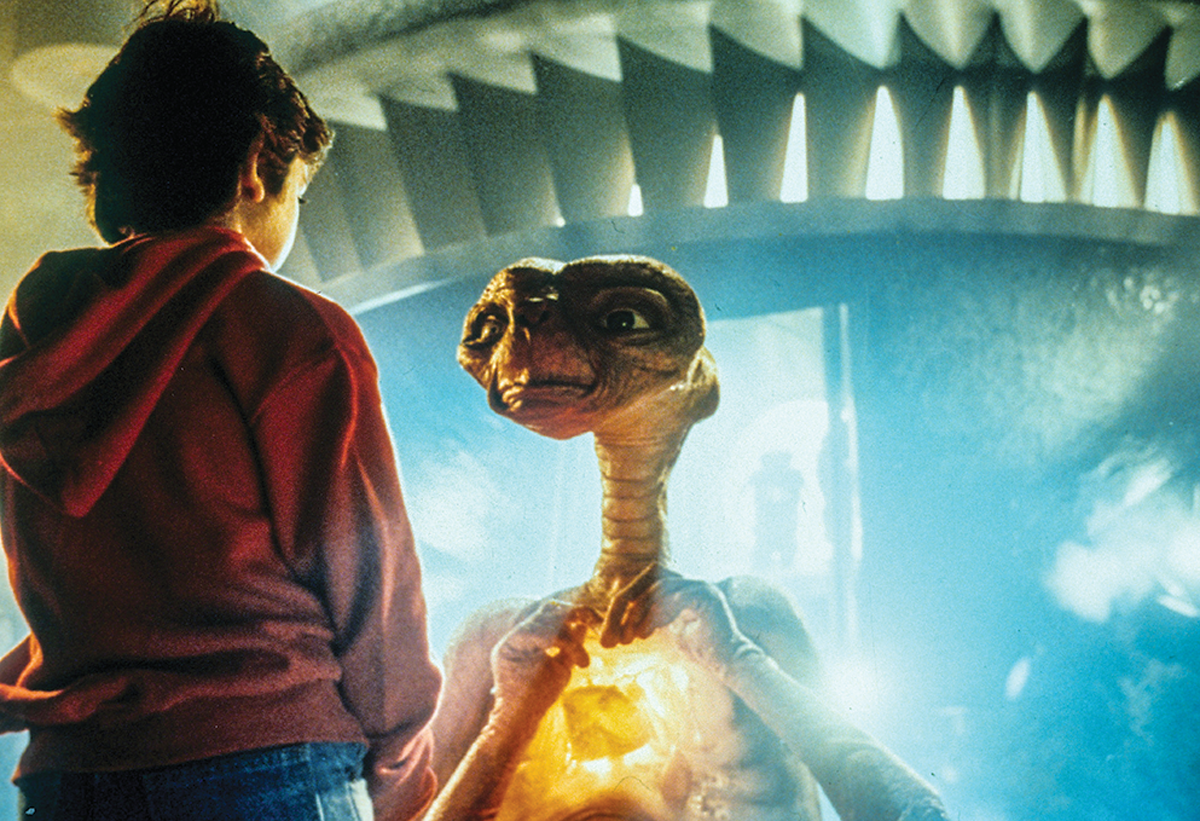 movie still of boy talking to E.T. with glowing chest and UFO behind