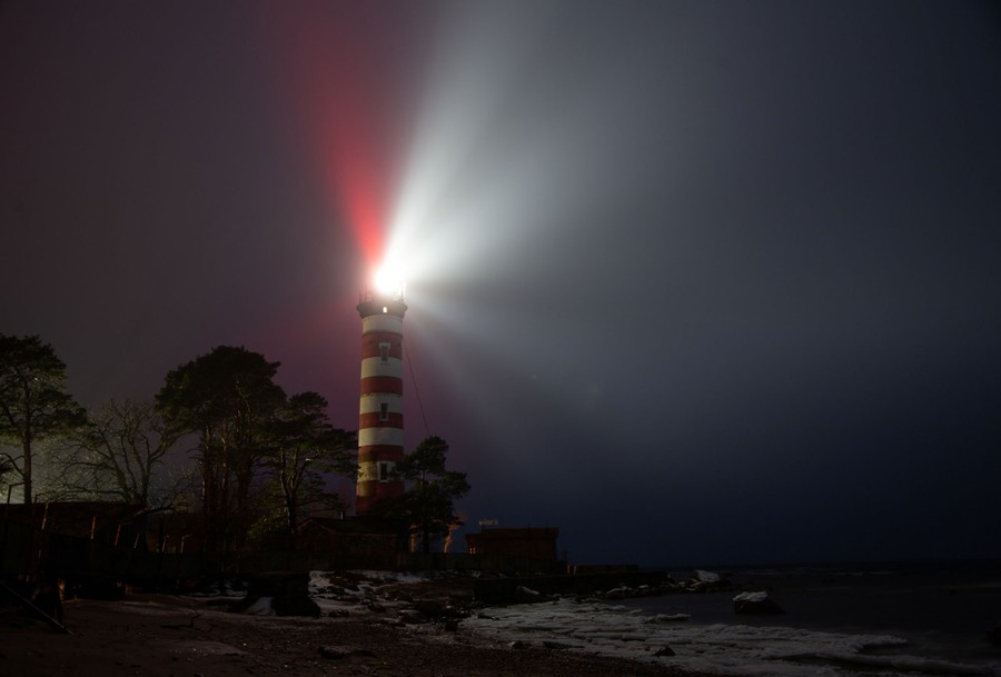 A red-and-white striped lighthouse is seen shining on a foggy night.