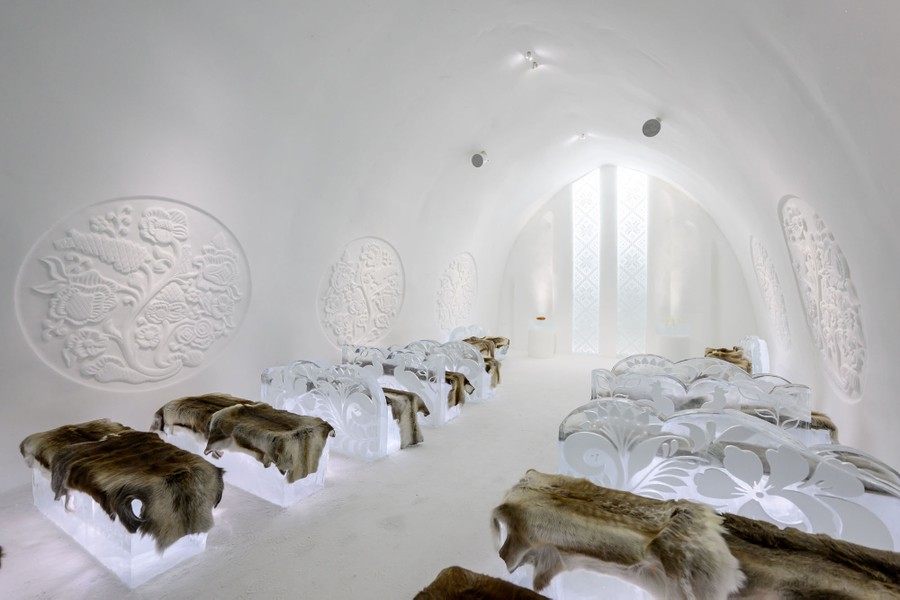 Những chiếc chăn lông nằm trên những chiếc ghế băng làm bằng băng bên trong một căn phòng được tạc bằng tuyết.