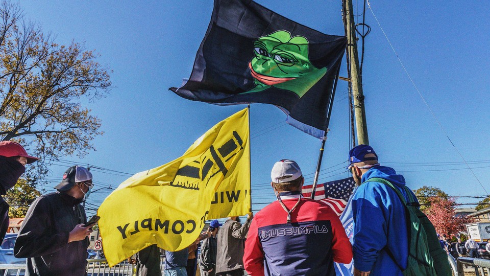 A color photo of a group of protesters carry flags, including an American one and a "Groyper" flag, which shows Pepe the frog on a black background.