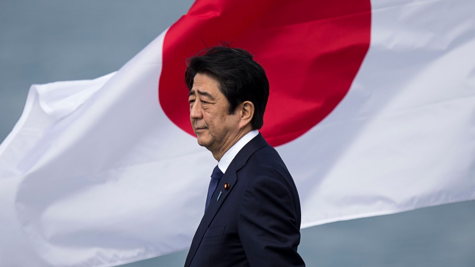 Former Japanese Prime Minister Shinzo Abe, wearing a navy suit and standing in front of the Japanese flag