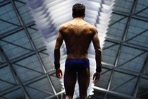 A diver wearing a swimsuit stands ready to jump, seen from behind.