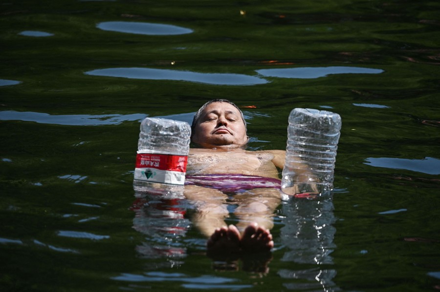 A man floats in a body of water, partially held up by two empty plastic bottles.