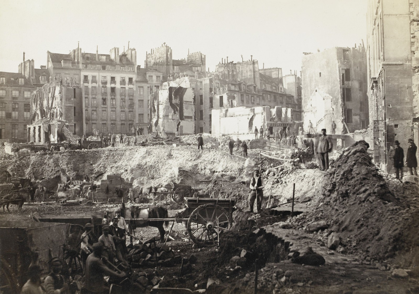 Many workers stand in and around an excavation site and several partially-demolished buildings.