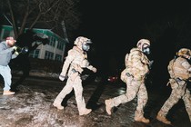 A man with a megaphone chases three ICE agents in a neighborhood at dusk