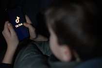 A 12-year-old boy looks at a smartphone screen displaying the TikTok logo