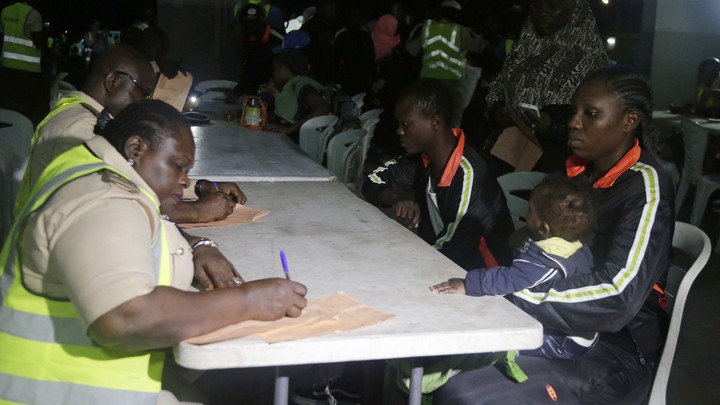 Nigerian returnees wait as Nigeria immigration officials fill out their return forms on folding tables.