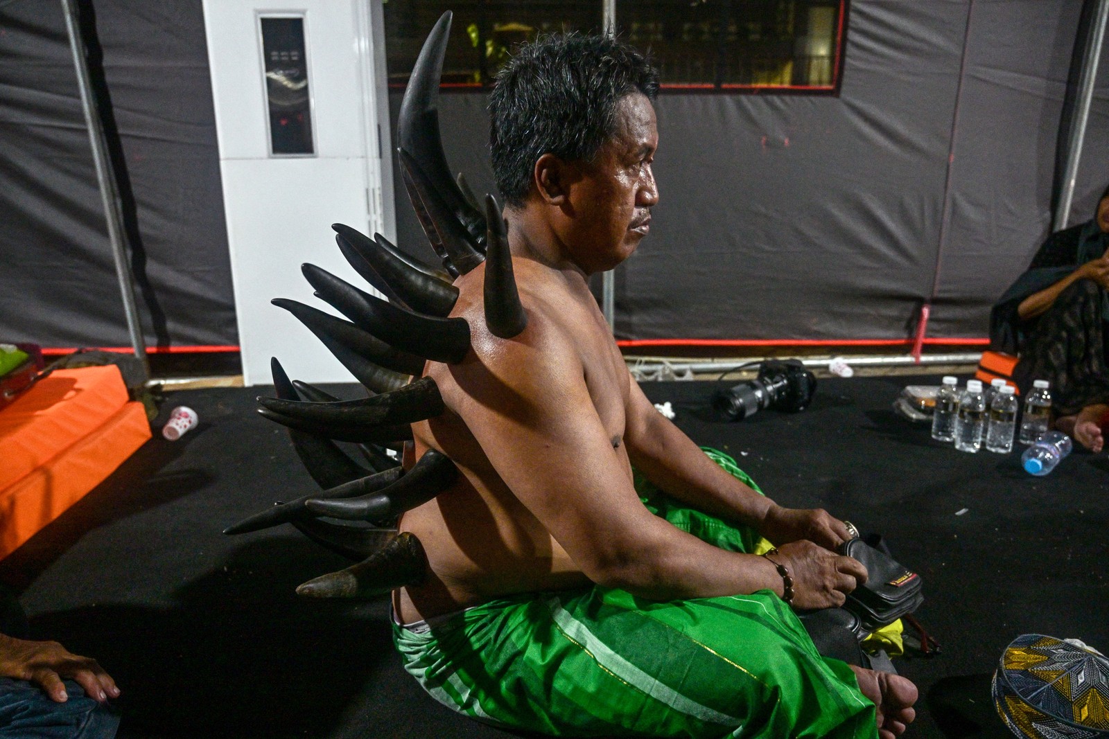 A man receives cupping therapy using cow horns, making it appear as if he has many horns poking out of his back and shoulders.