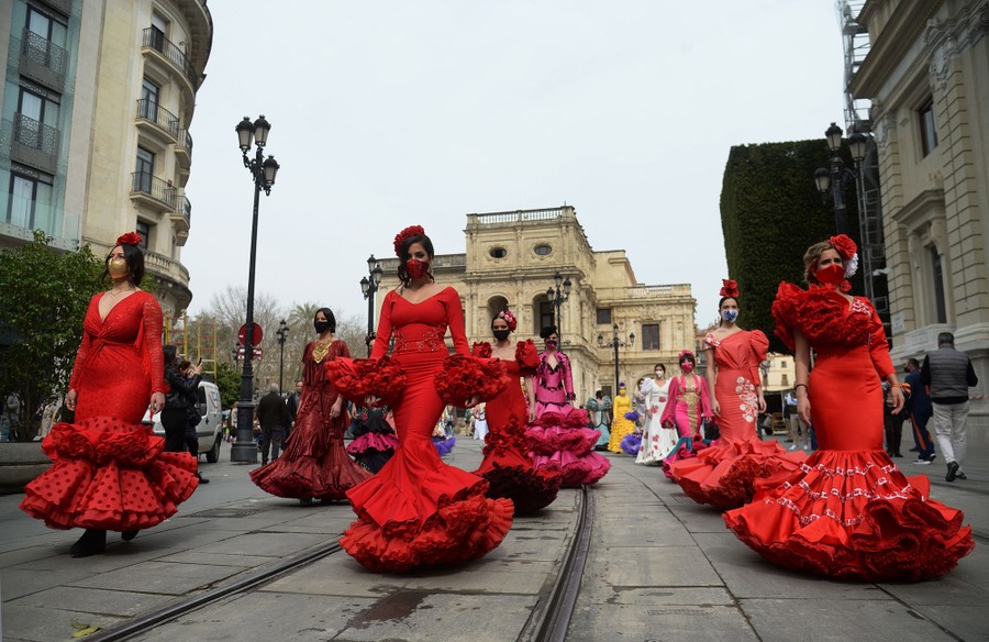 Many people march in a street, wearing traditional bright red dresses.