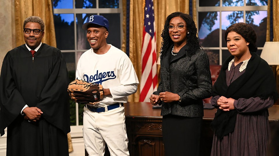Four Black people stand smiling in a replica of the oval office. From left: a man wearing a judge's robe and glasses, a man dressed in a Dodgers baseball uniform, a woman with glasses wearing a black suit, and a woman wearing a dress with a lace collar and a shawl