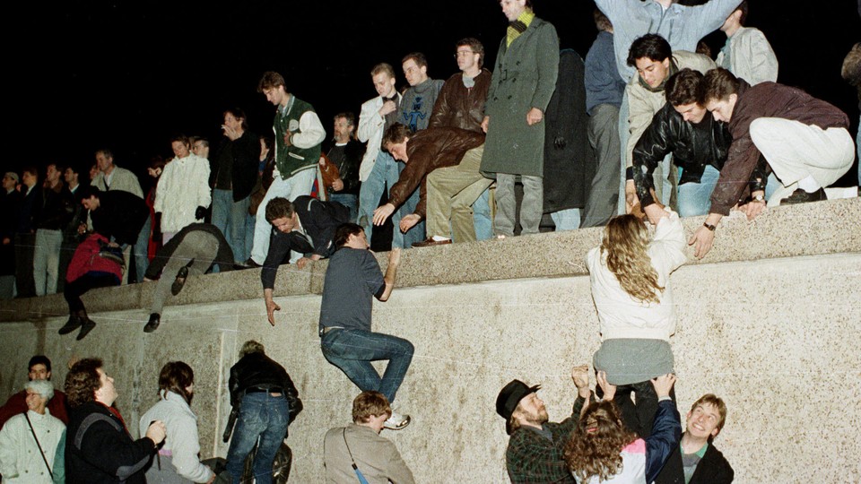 East German citizens climb the Berlin wall at the Brandenburg Gate as they celebrate the opening of the East German border on November 10, 1989.