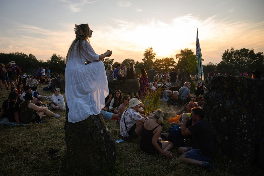 A woman in a long dress sits on a large stone among many concertgoers.