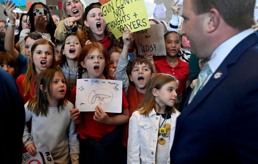 A group of young students holding protest signs shout at state lawmakers inside a state capitol.