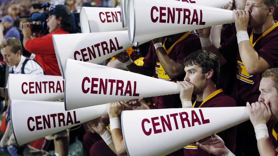People hold megaphones that read "CENTRAL" along the side in the stands of a football game.