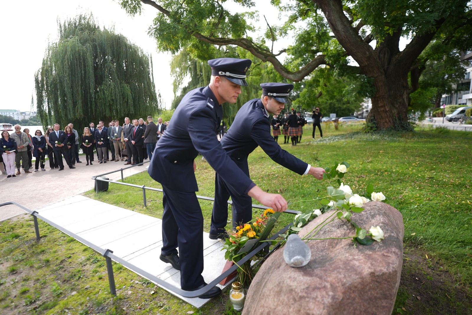 Two firefighters lay flowers at a memorial stone during a ceremony.