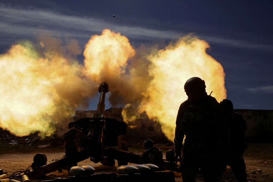 Soldiers fire a large piece of artillery, sending plumes of fire and smoke in several directions.