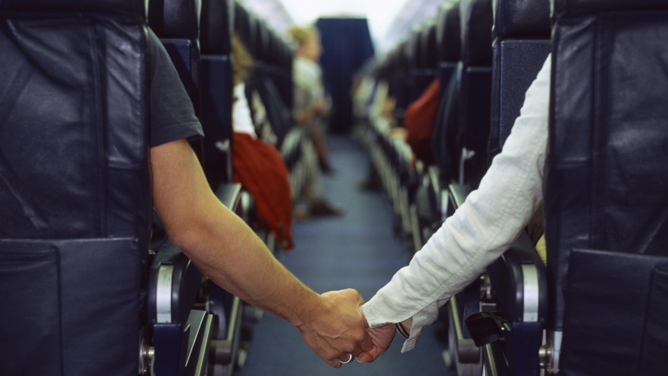 Two people hold hands across an airplane aisle