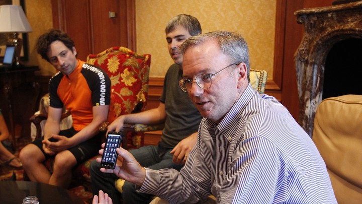 One man holds up an Android phone while two others look on.