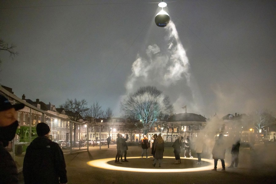 People stand in a public square at night, looking up toward an artwork made from a 3-foot sphere and a powerful light.